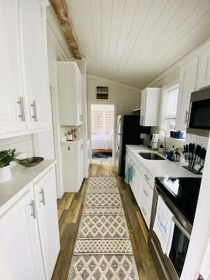 A narrow kitchen with white cabinets, a black refrigerator, and a microwave. A patterned rug runs down the center of the floor.