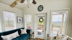 A cozy living room with a teal sofa, a beige sofa, and a wooden coffee table. A clock is mounted on the wall, and a wreath hangs on the door. - Luxury Tiny Home with River Views on 300 Acre Ranch (Decatur)