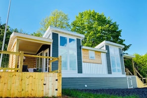 A modern mobile home with a covered porch, a small deck, and a front entrance.