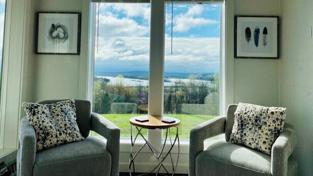 A room with two armchairs, a small round table, and a large window offering a view of a landscape. - Luxury Tiny Home with River Views on 300 Acre Ranch (Decatur)