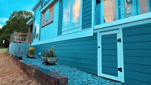 A two-story house with a blue exterior, large windows, and a front porch with planters. - Luxury Tiny Home with River Views on 300 Acre Ranch (Decatur)