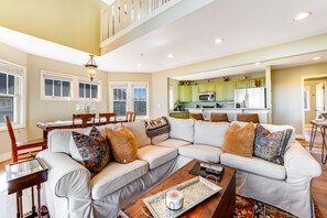 A spacious living room with a large sectional sofa, a dining area with a table and chairs, and a kitchen with green cabinets and modern appliances.