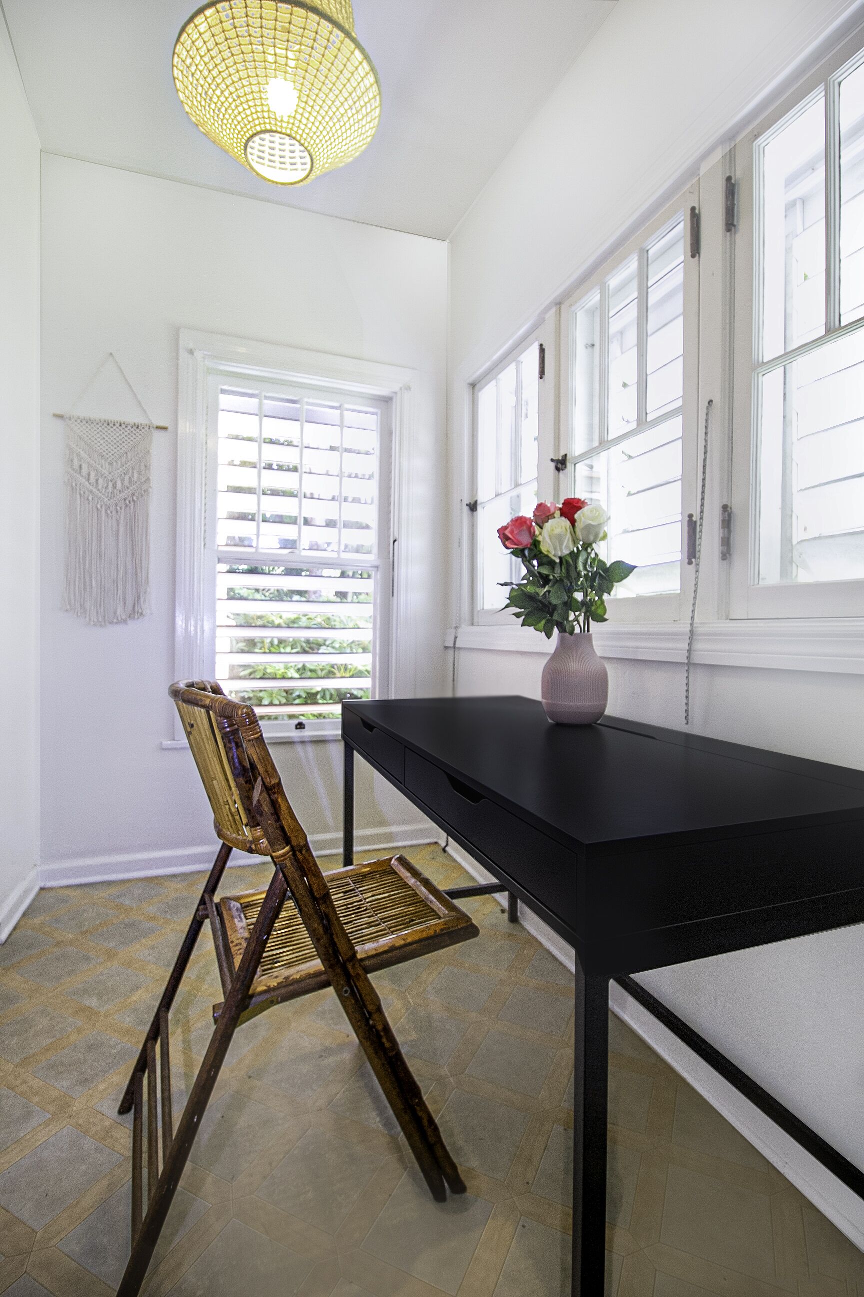 A room with a black table, a chair, a vase with flowers, and a window with blinds.