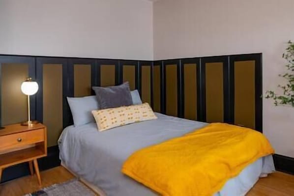 Ein Schlafzimmer mit einem Bett, einem Nachttisch, einer Lampe und einer Pflanze.