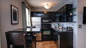 A compact kitchen with dark cabinetry, a stainless steel refrigerator, a microwave, and a built-in oven. There is a small countertop with a toaster and a sink. - Amazing Uptown Studio long stays (Minneapolis)