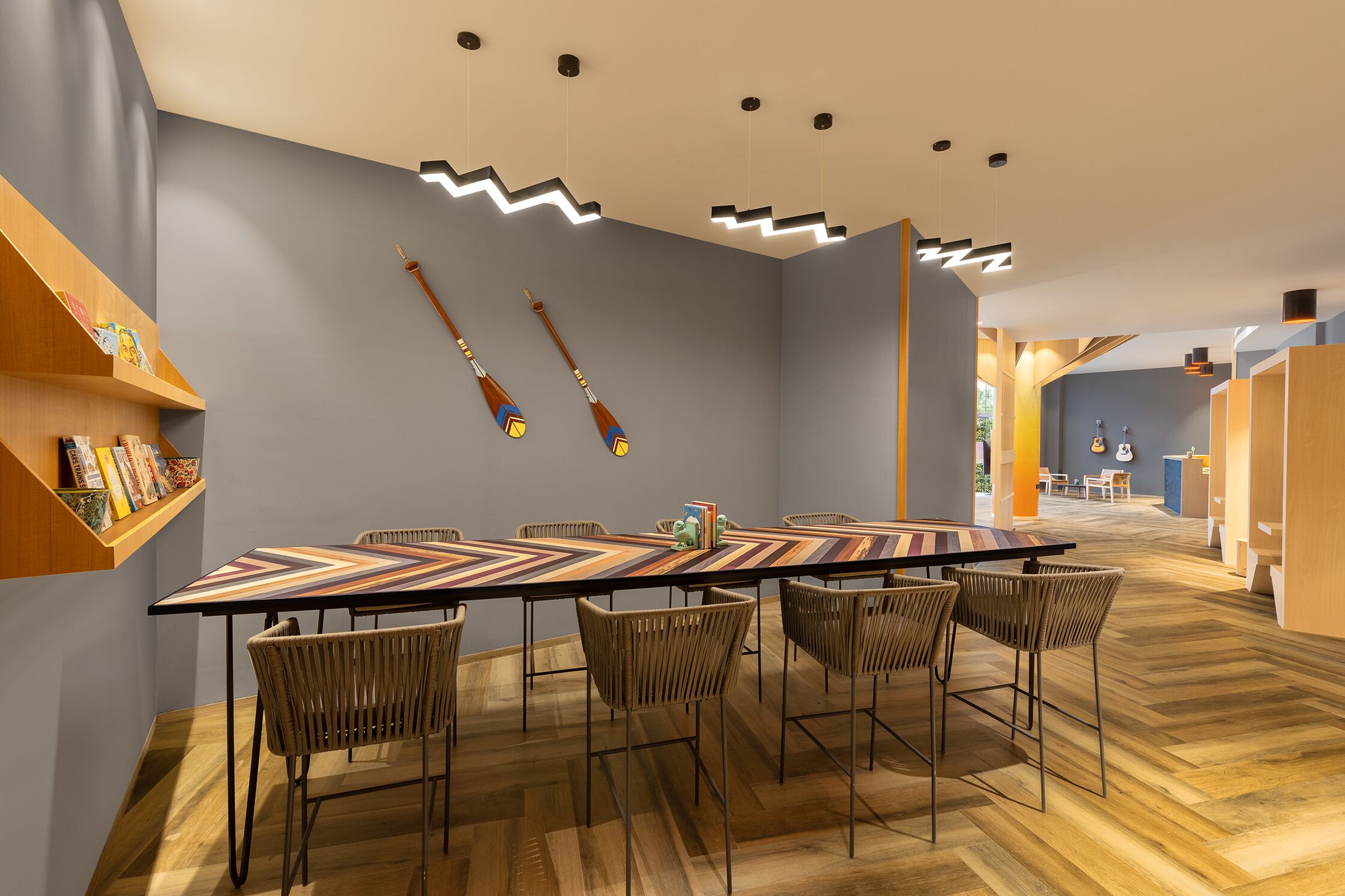 A modern dining area with a long table, wicker chairs, and a wooden floor.