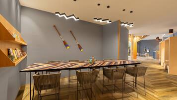 A modern dining area with a long table, wicker chairs, and a wooden floor.