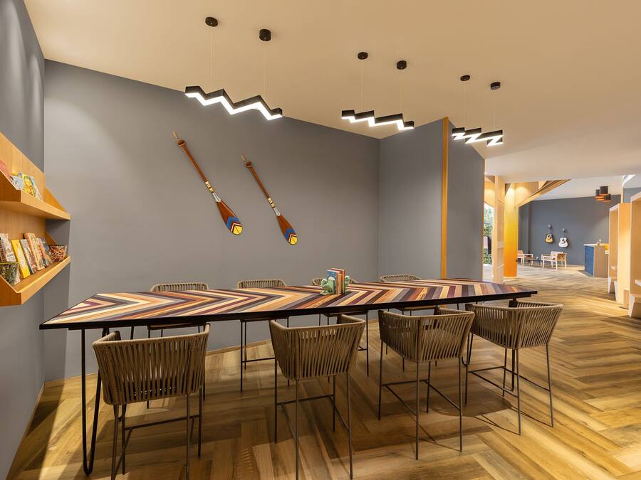 A modern dining area with a long table, wicker chairs, and a wooden floor.