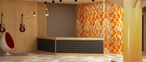 Un espace d’accueil moderne avec un comptoir de réception en bois, un mur aux motifs géométriques colorés et un fauteuil rouge et blanc original.