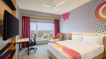 Habitación de hotel con una cama grande, un escritorio, una silla, un televisor y vistas de la ciudad.