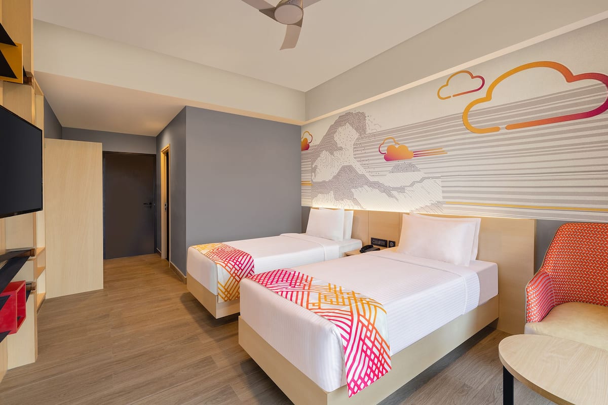 A hotel room with two beds, a desk, a chair, a TV, and a ceiling fan.