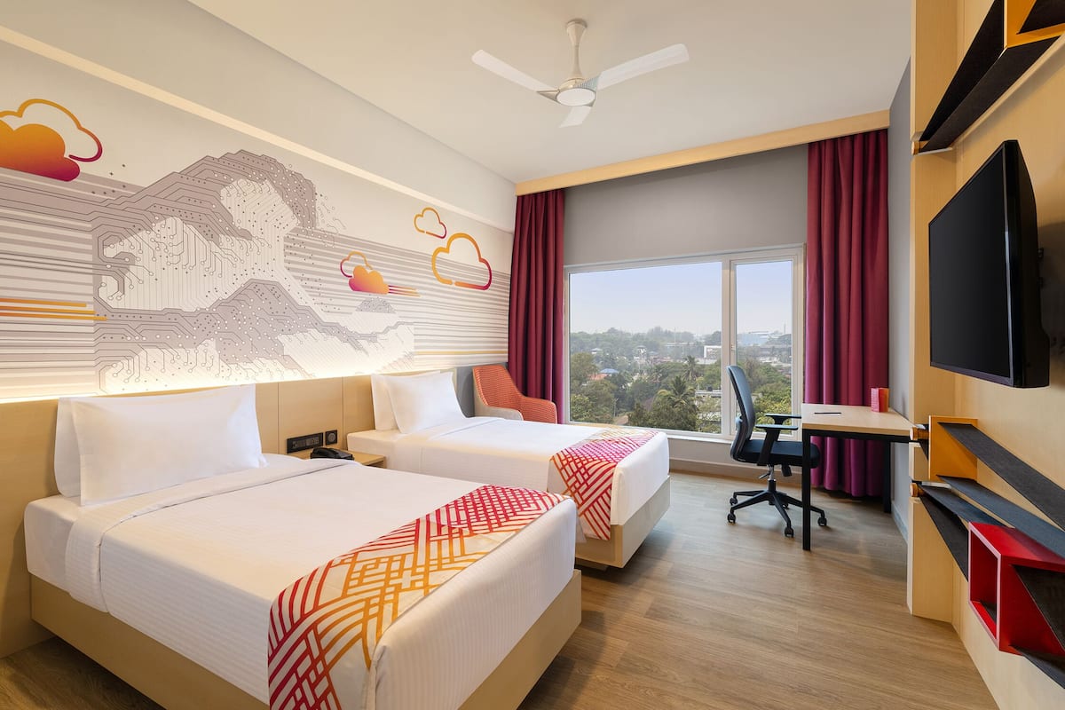 A hotel room with two beds, a desk, a chair, a TV, and a large window with a city view.