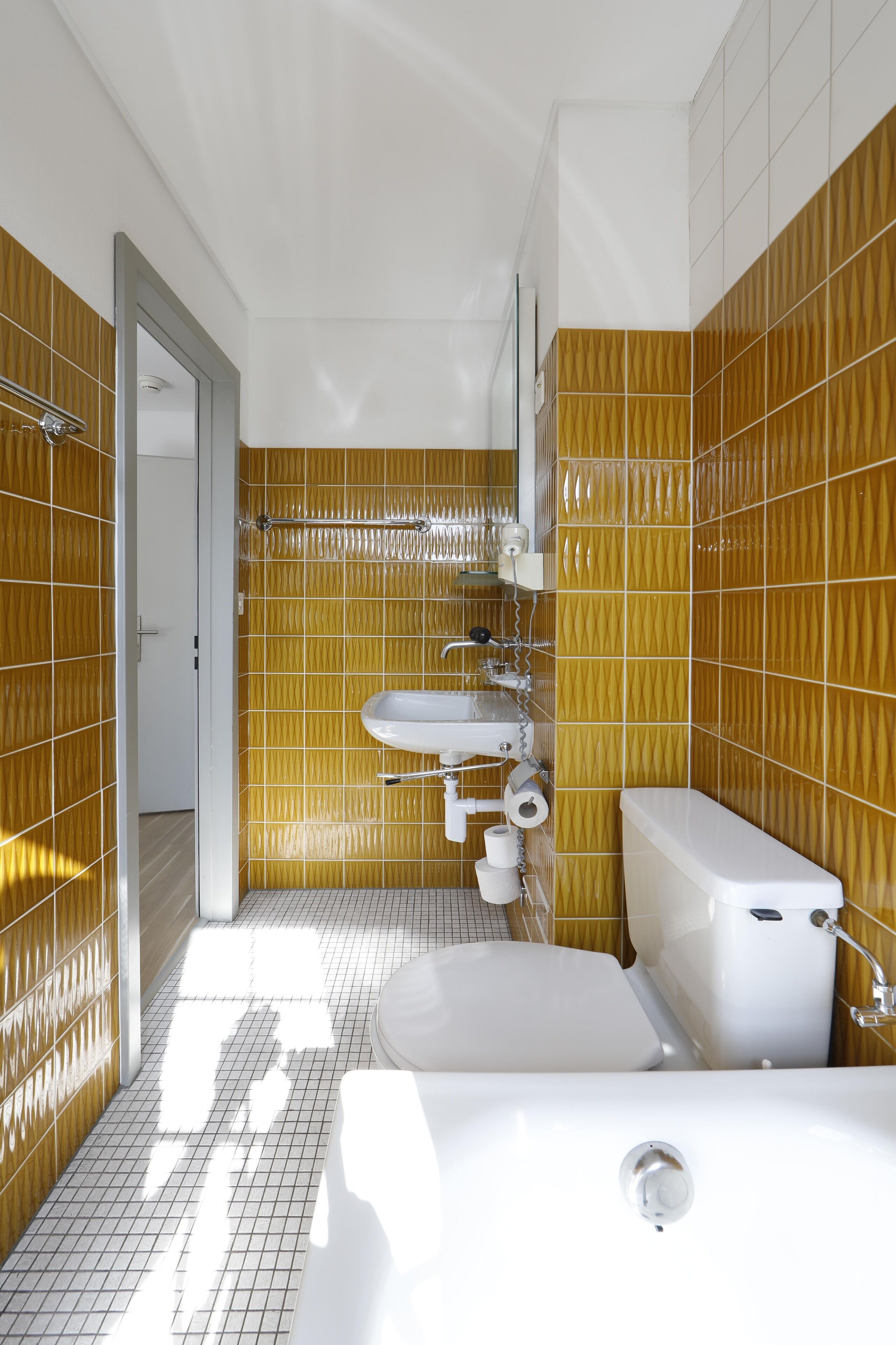 A bathroom with a white sink, toilet, and bathtub, with yellow patterned walls and a tiled floor.