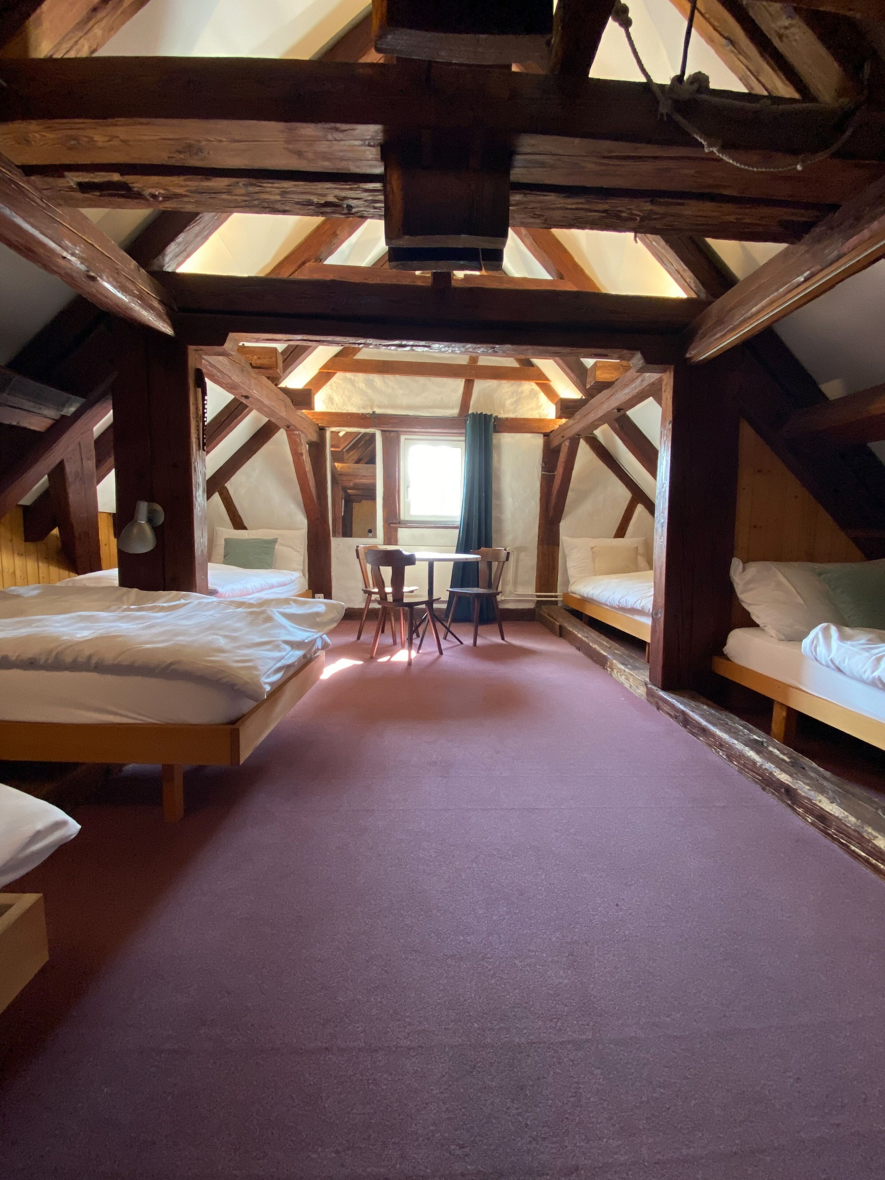 A cozy attic bedroom with two beds, a small table, and a chair.