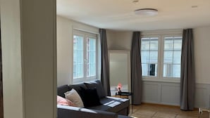 A modern living room with a grey sofa, a small side table, and a window with curtains. - Hotel Untertor by Maier Self-Check-in (Altstaetten)