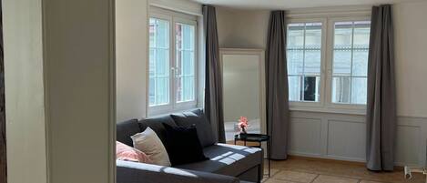 A room with a sofa, a small table, and a window with curtains.