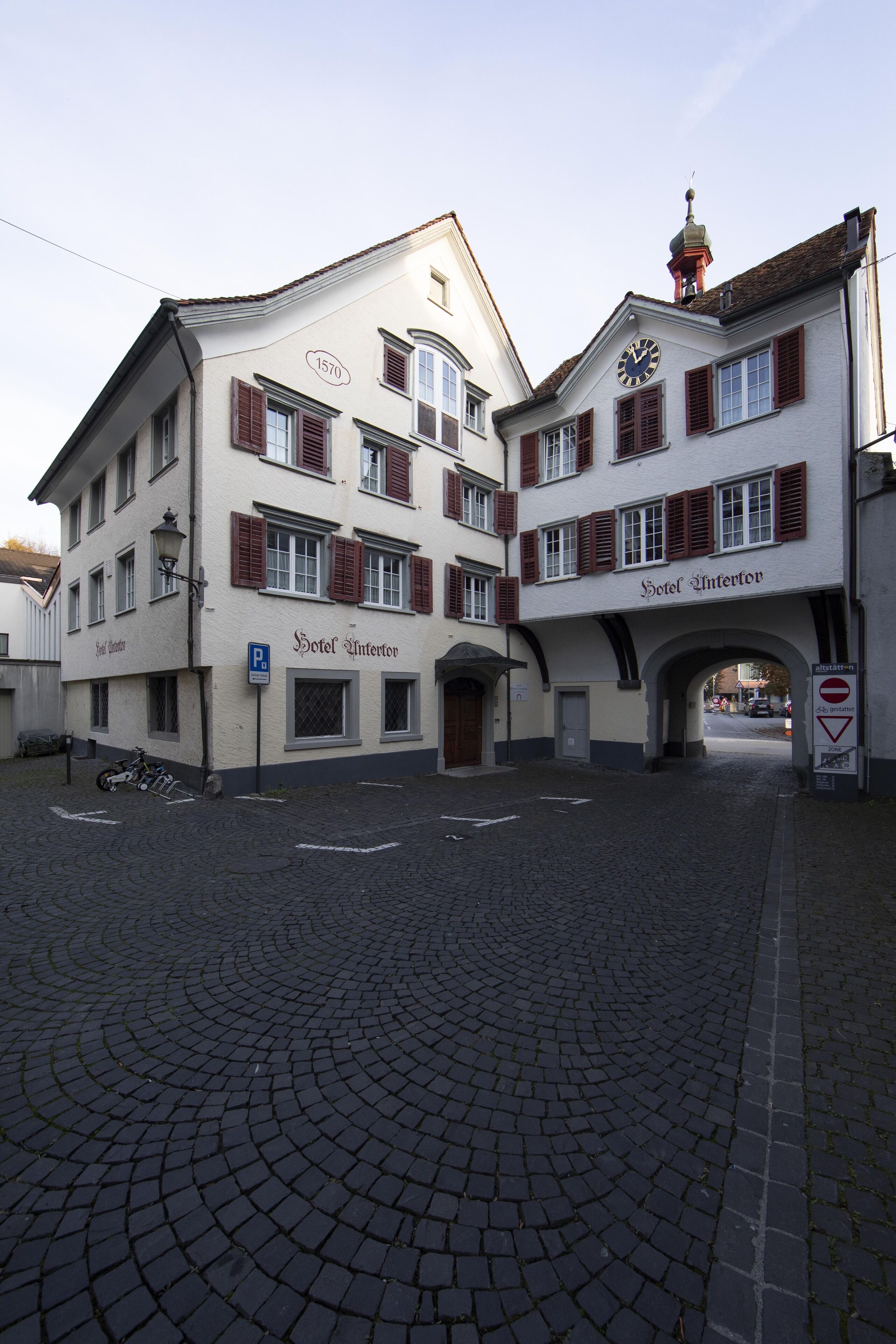 Ein historisches Gebäude mit einem Uhrturm, einem Schild mit der Aufschrift 'Hotel Intertor' und einer Kopfsteinpflasterstraße.