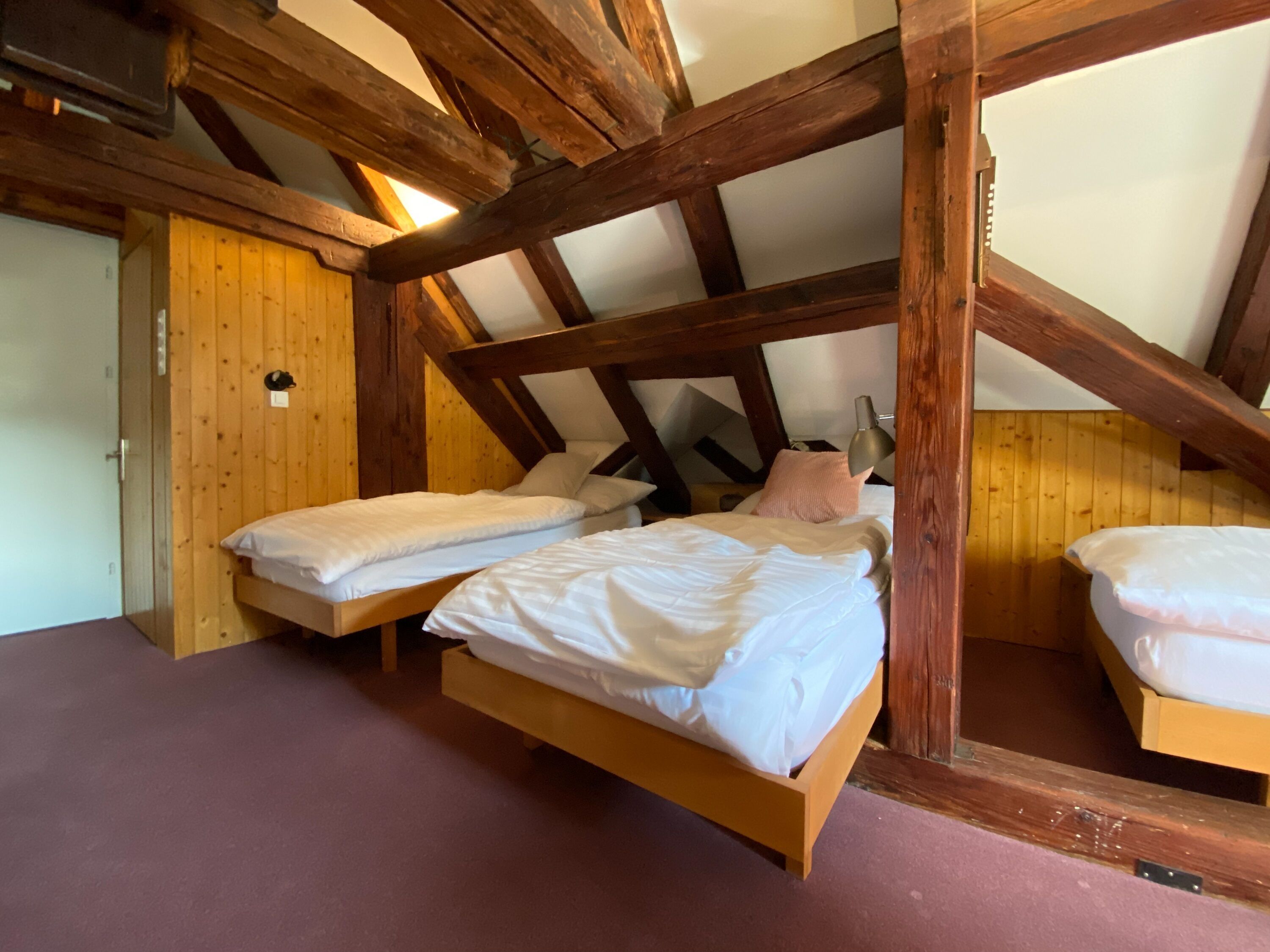 Ein Zimmer mit zwei Betten, Holzbalken und einer geneigten Decke.