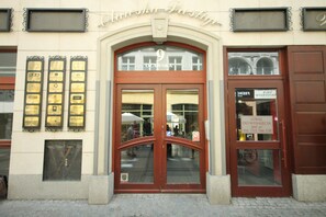 A building entrance with a large arched doorway, plaques on the wall, and a sign with contact information.