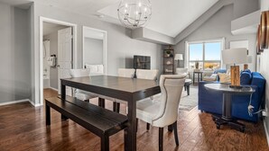 A modern living room with a dark wooden dining table, white upholstered chairs, a blue sofa, and a chandelier. - Luxury | Comfort | Pool | Hot Tub | Gym (Invermere)