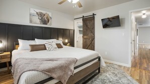A bedroom with a large bed, a ceiling fan, a mounted TV, and a barn door sliding door. - Charming 3bed/2 bath near Gathering Place, Riverparks and Downtown (Tulsa)