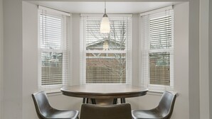 A corner dining area with a round table and two chairs, large windows with blinds, and a hanging light fixture. - Charming 3bed/2 bath near Gathering Place, Riverparks and Downtown (Tulsa)