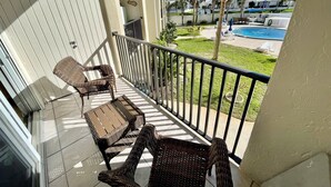 Un balcon agrémenté de meubles en osier, une piscine et des palmiers en arrière-plan.