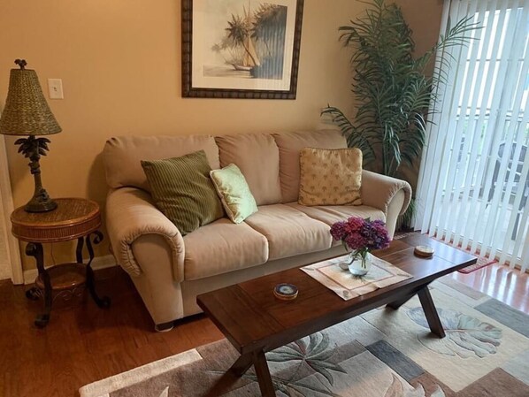 Una sala de estar con un sofá color beige, una mesa de centro de madera, una lámpara y un cuadro enmarcado en la pared.