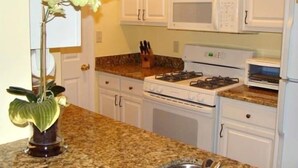 A kitchen with white cabinets, a granite countertop, a stove, a microwave, and a sink. - Reasonable  Rates: Beautiful Condo Close to Beach, Restaurants, Shopping & More! (Rehoboth Beach)