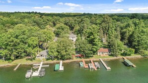 Propiedad frente al lago con barcos amarrados, una casa pequeña y un bosque denso al fondo.