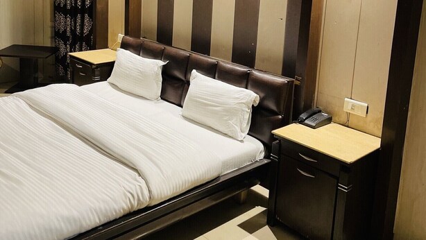 A hotel room with a large bed, two bedside tables, a telephone, and a wall-mounted light fixture. - Hotel R S Residency (Amritsar)