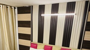 A bed with white bedding, a headboard with pink and beige cushions, and striped curtains. - Hotel R S Residency (Amritsar)