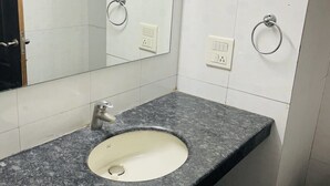 A bathroom with a granite countertop sink, a mirror, and two towel rings. - Hotel R S Residency (Amritsar)