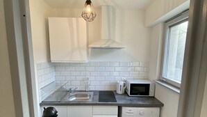 A compact kitchen with white cabinets, a microwave, a kettle, and a washing machine. - New Studio - City Center Mulhouse - Near Train station (Mulhouse)