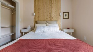 Ein Schlafzimmer mit Bett, Holz-Kopfteil, Nachttisch mit Lampe, kleinem Tisch mit Schale und einem gerahmten Bild an der Wand.