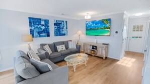 Ein Wohnzimmer mit grauem Sofa, einem Glastisch und zwei an der Wand hängenden Bildern.