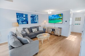 A living room with a grey sofa, a glass coffee table, and two wall-mounted paintings. - Spectacular Beach House just 1 min. walk to beach w/ Private Salt Pool & Hot Tub (Surfside Beach)