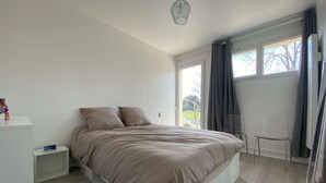 A bedroom with a bed, a nightstand, a chair, and a window with curtains. - #Casafouilloy Apartment with large terrace (Fouilloy)