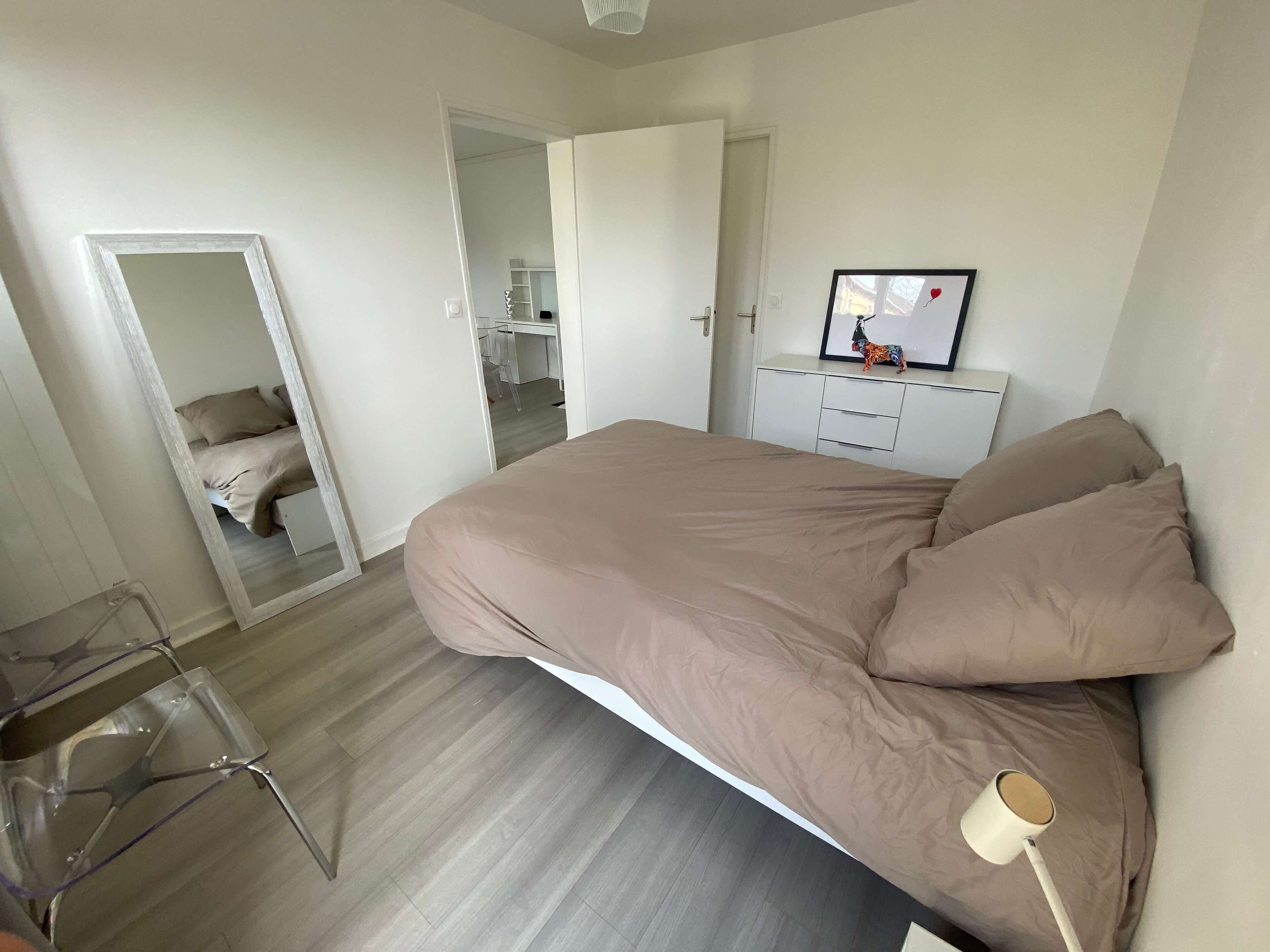 Een slaapkamer met een bed, een dressoir, een spiegel en een stoel.