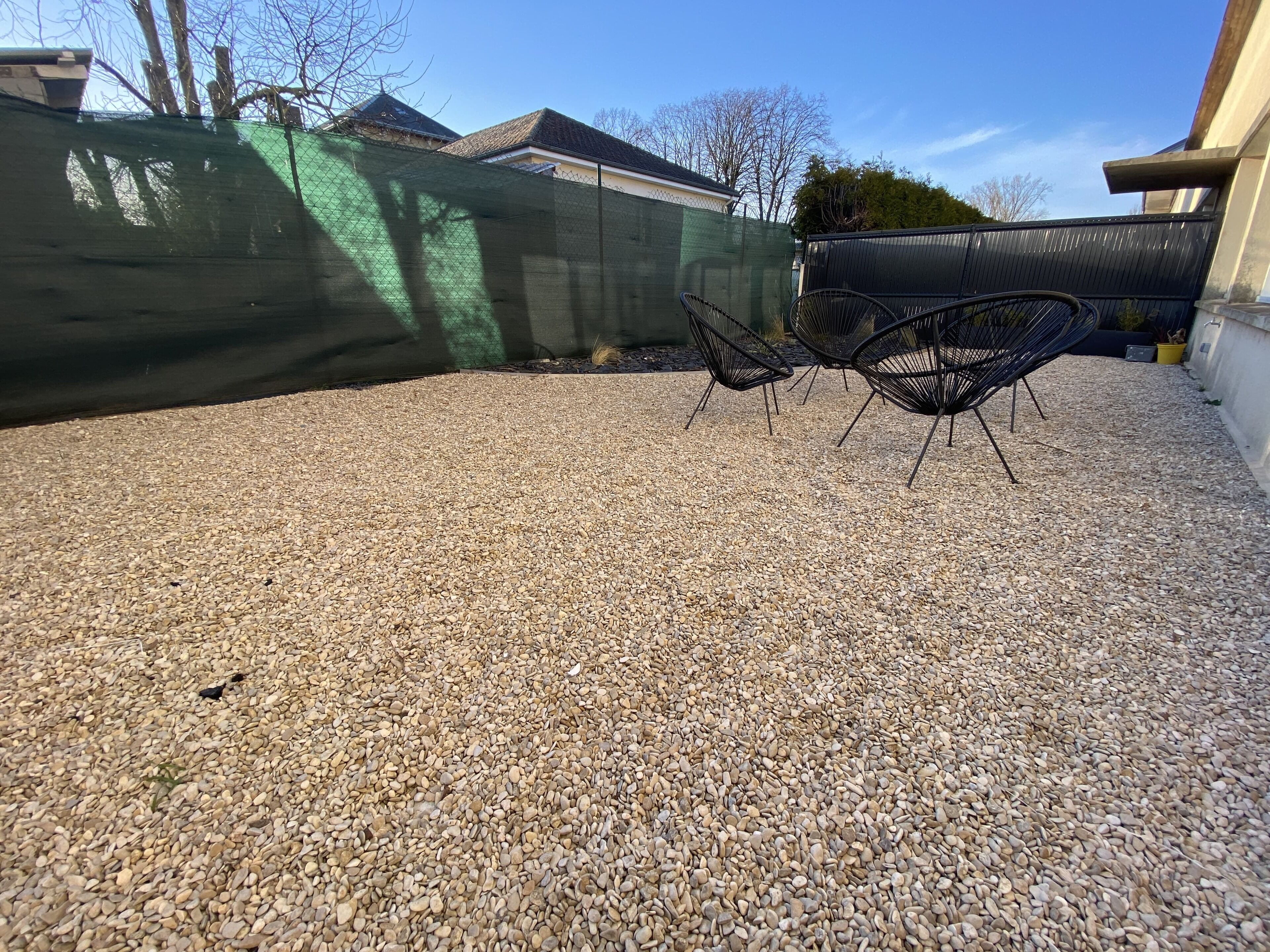 Une terrasse en gravier avec une chaise en métal noir et une table en métal noir.