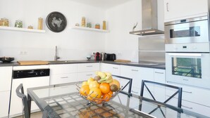 A modern kitchen with white cabinetry, stainless steel appliances, and a glass dining table with a fruit bowl. - Detached house + private pool located 5 mn from Avignon and 15 mn from St Rémy (Les Angles)