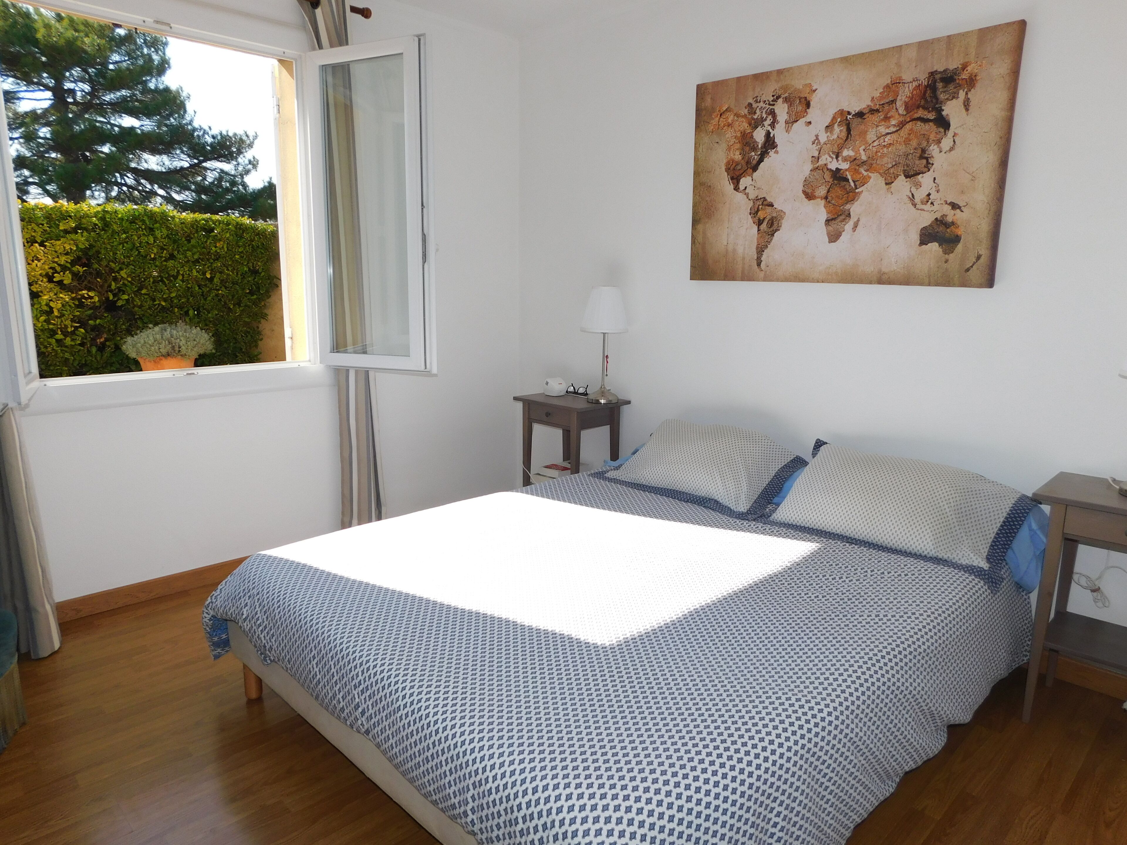 Une chambre à coucher avec un lit, une table de chevet, une lampe, une fenêtre et une carte du monde accrochée au mur.