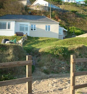 Situated on a sloped terrain, this two-story house offers a serene residential setting with a grassy yard and a sandy area.