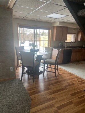 A dining area with a round table and chairs, a kitchen with wooden cabinets, and a large window providing natural light. - Holistic Hideaway (Cheboygan)