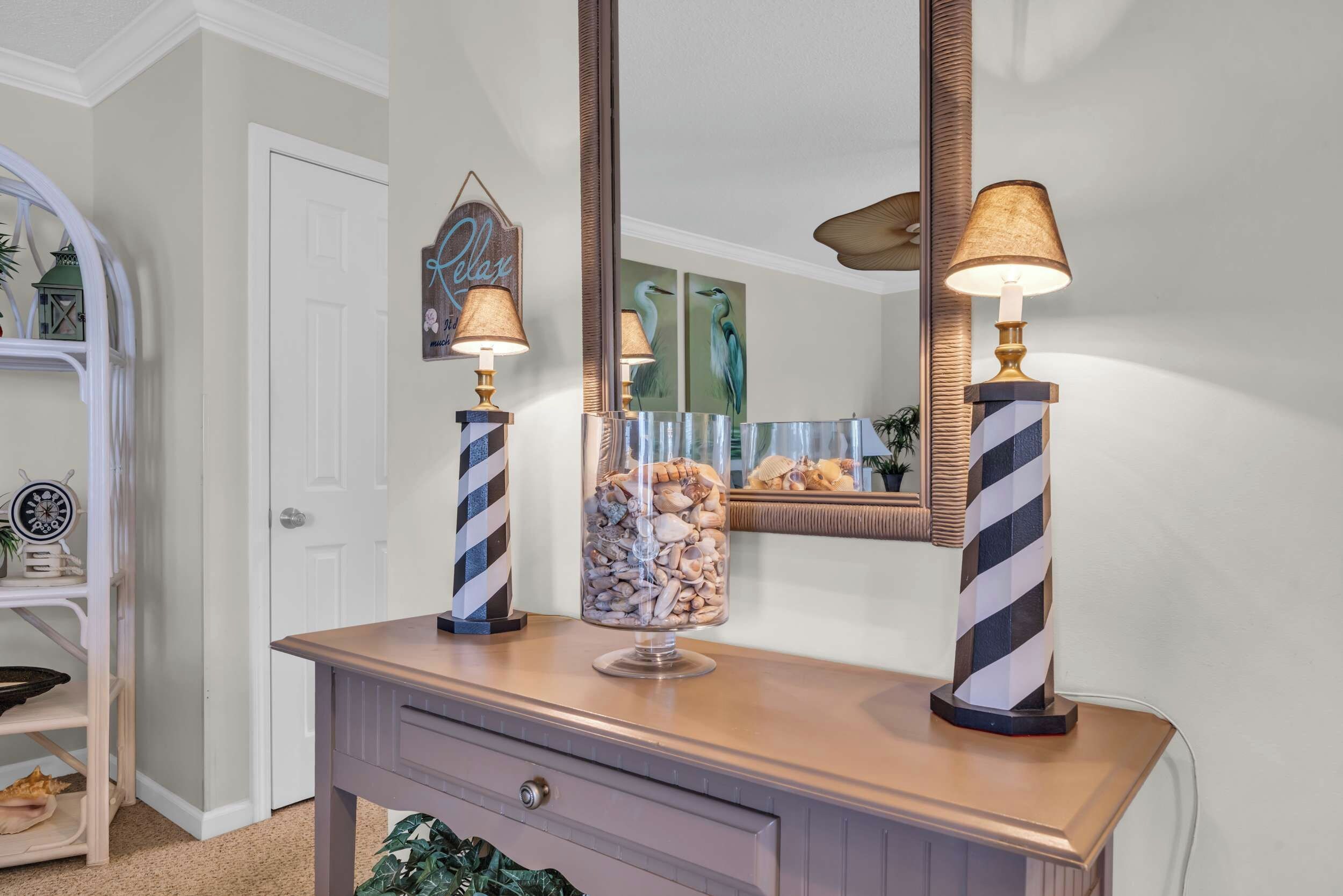 A vanity with two striped lamps, a decorative mirror, and a glass jar with seashells.