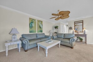 A living room with a sectional sofa, a coffee table, a lamp, and two wall-mounted paintings. - Shorehaven Lakefront & Steps to Beach w Pool (North Myrtle Beach)