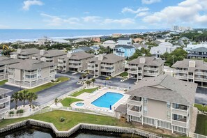 A residential area with a swimming pool surrounded by a white fence, a dock, and a view of the ocean. - Shorehaven Lakefront & Steps to Beach w Pool (North Myrtle Beach)