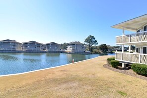 A waterfront property with multiple apartment buildings, a grassy area, and a small bridge. - Shorehaven Lakefront & Steps to Beach w Pool (North Myrtle Beach)