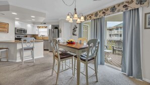 Una cocina moderna con armarios blancos, una isla central y un comedor con mesa y sillas de madera.