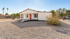 Una casa moderna de un piso con una puerta roja, un porche pequeño y un camino de entrada de grava.